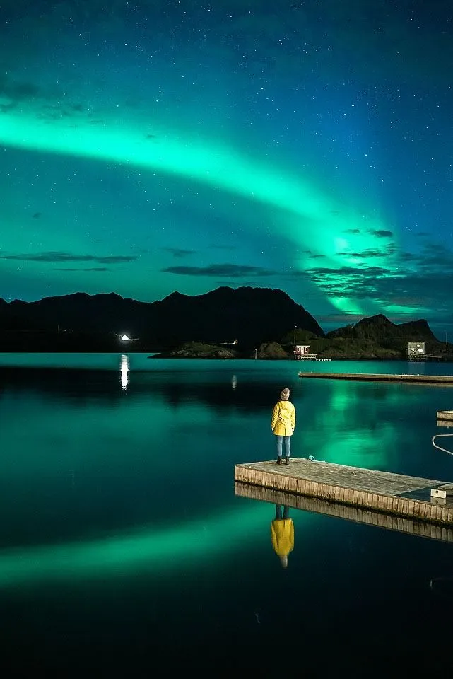 Person som ser utover fjorden med nordlys over seg.